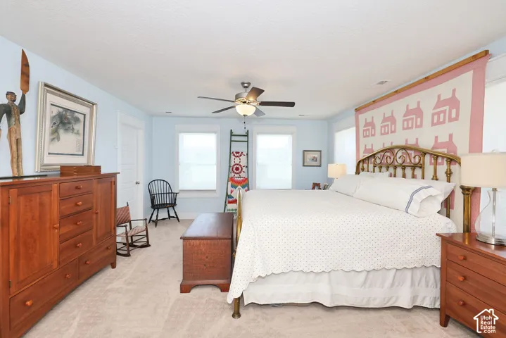 Carpeted bedroom featuring a ceiling fan with integrated lighting, two windows with blinds, a white door, and light blue walls