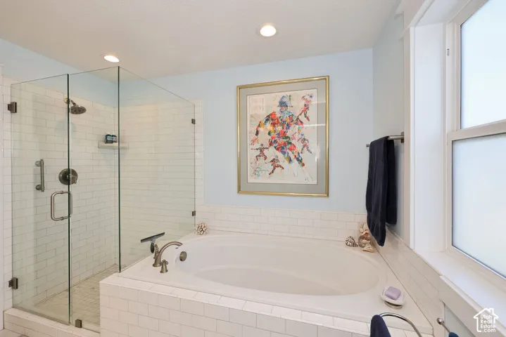 Spacious bathroom featuring an integrated soaking tub, a frameless glass shower enclosure with subway tile surround, recessed lighting, and a window with privacy glass