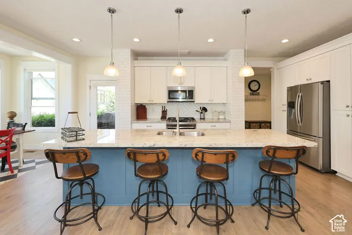 Kitchen featuring a blue-toned island with seating, pendant lighting, light-toned cabinetry, stainless steel appliances, and wood-finish flooring