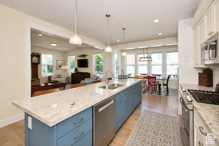 Kitchen featuring an expansive island with a light-toned countertop, stainless steel appliances, blue-finish base cabinetry, and wood-finish flooring