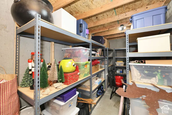 Expansive storage room featuring concrete walls, exposed wood ceiling joists, multiple metal shelving units, and concrete flooring