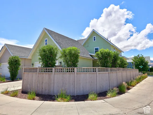 Corner property featuring a light green exterior, a dark shingle roof, and a wood privacy fence with lattice top
