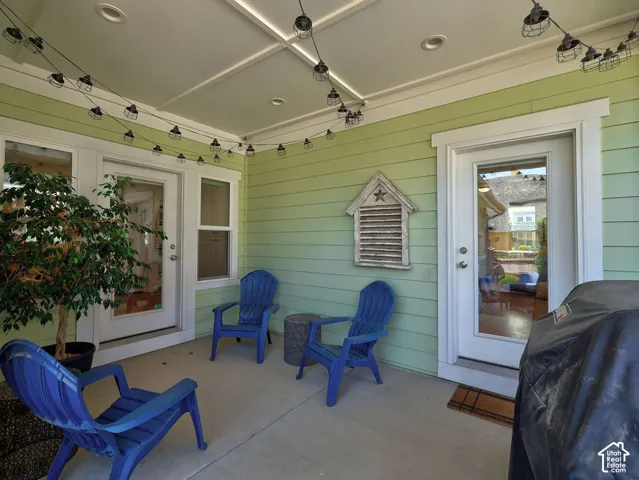 Covered concrete patio featuring recessed lighting and string lights, dual glass-paneled access doors, and light green horizontal siding