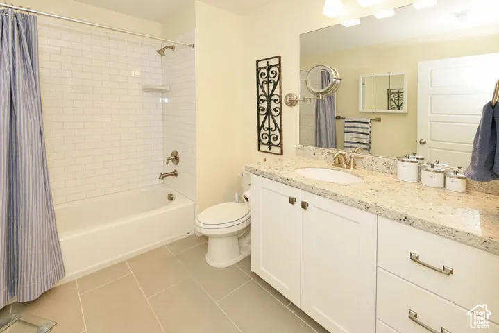 Bathroom featuring a white subway tile shower surround, a built-in tub, a single vanity with a light-colored speckled countertop, white cabinetry with brushed nickel hardware, and light gray floor tiles