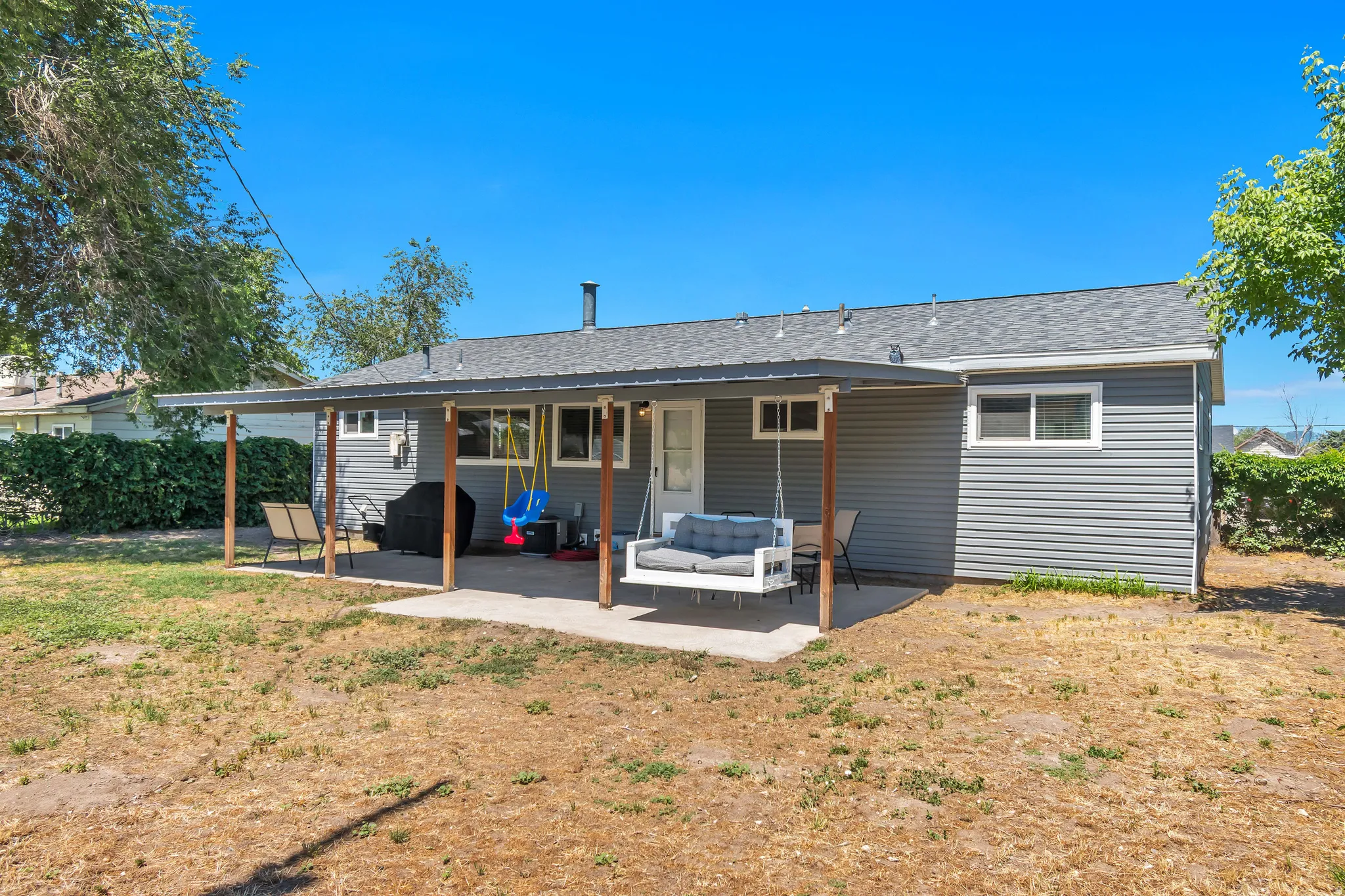 Rear exterior featuring grey horizontal siding and a shaded patio