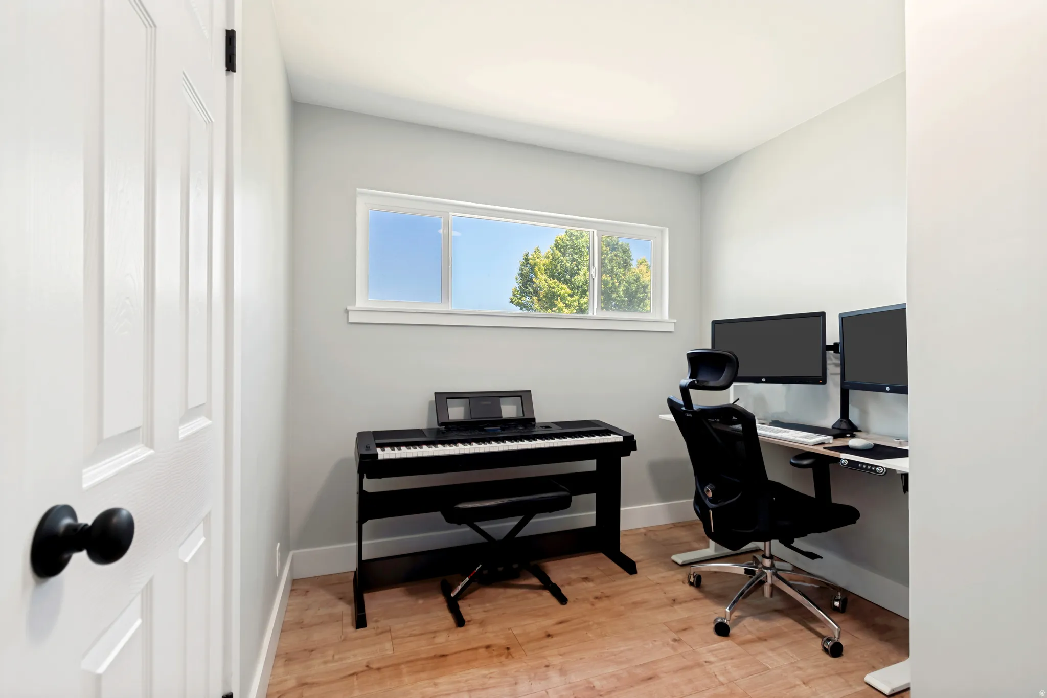Room with light wood-finish flooring, light gray wall paint, and white baseboards currently used as an office and music room