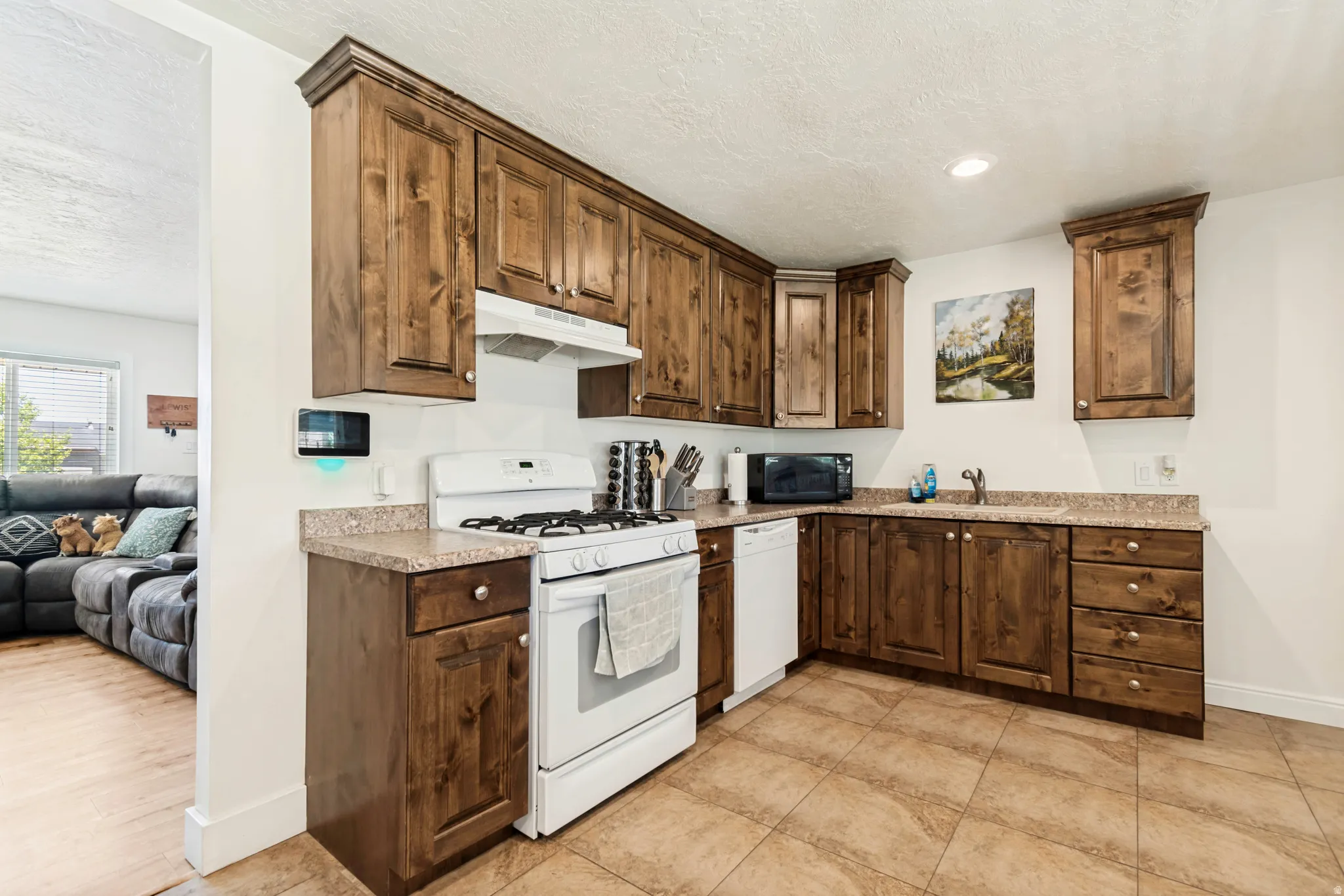 Open-concept kitchen featuring wood-finish cabinetry, a white gas range, and a built-in dishwasher