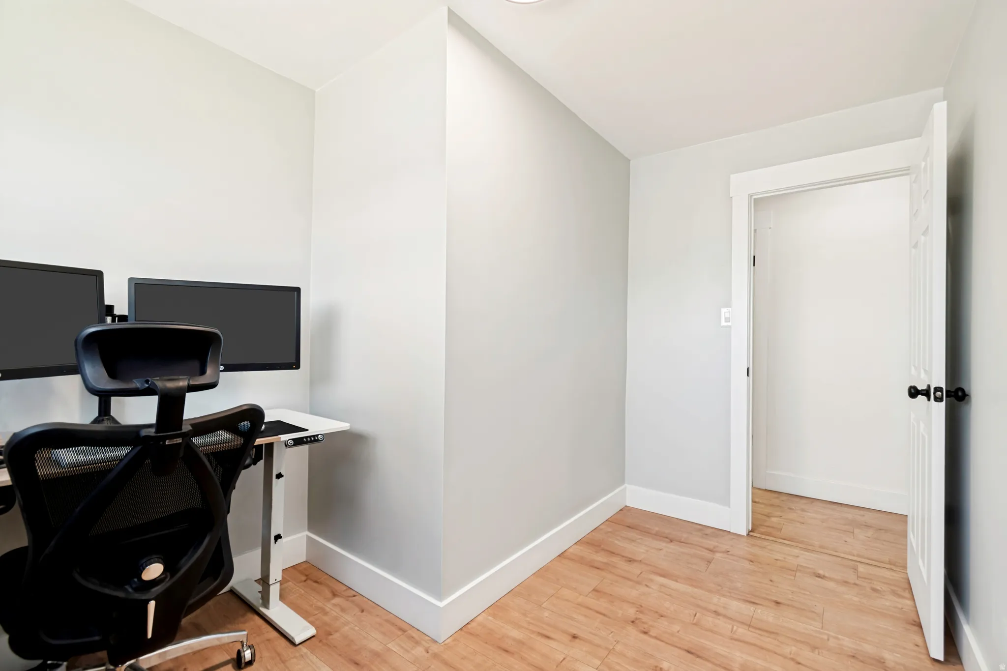 Room featuring wood-finish flooring, light gray walls, white trim, and a white paneled door with black hardware