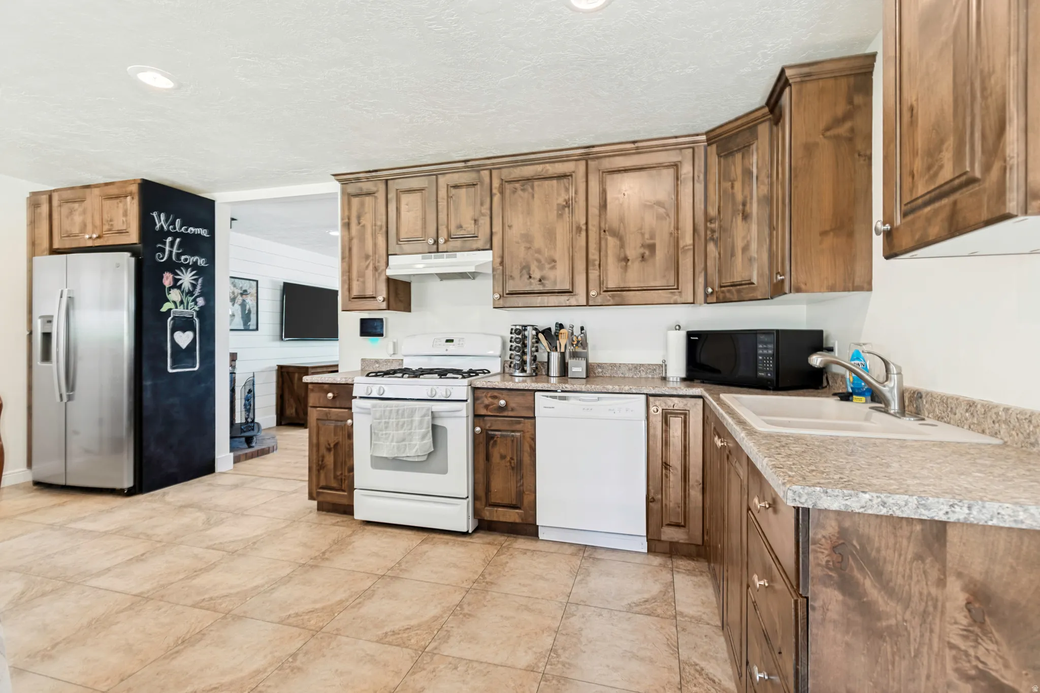 Kitchen featuring wood-finish cabinetry, light-toned countertops, tile flooring, a stainless steel refrigerator, and recessed lighting