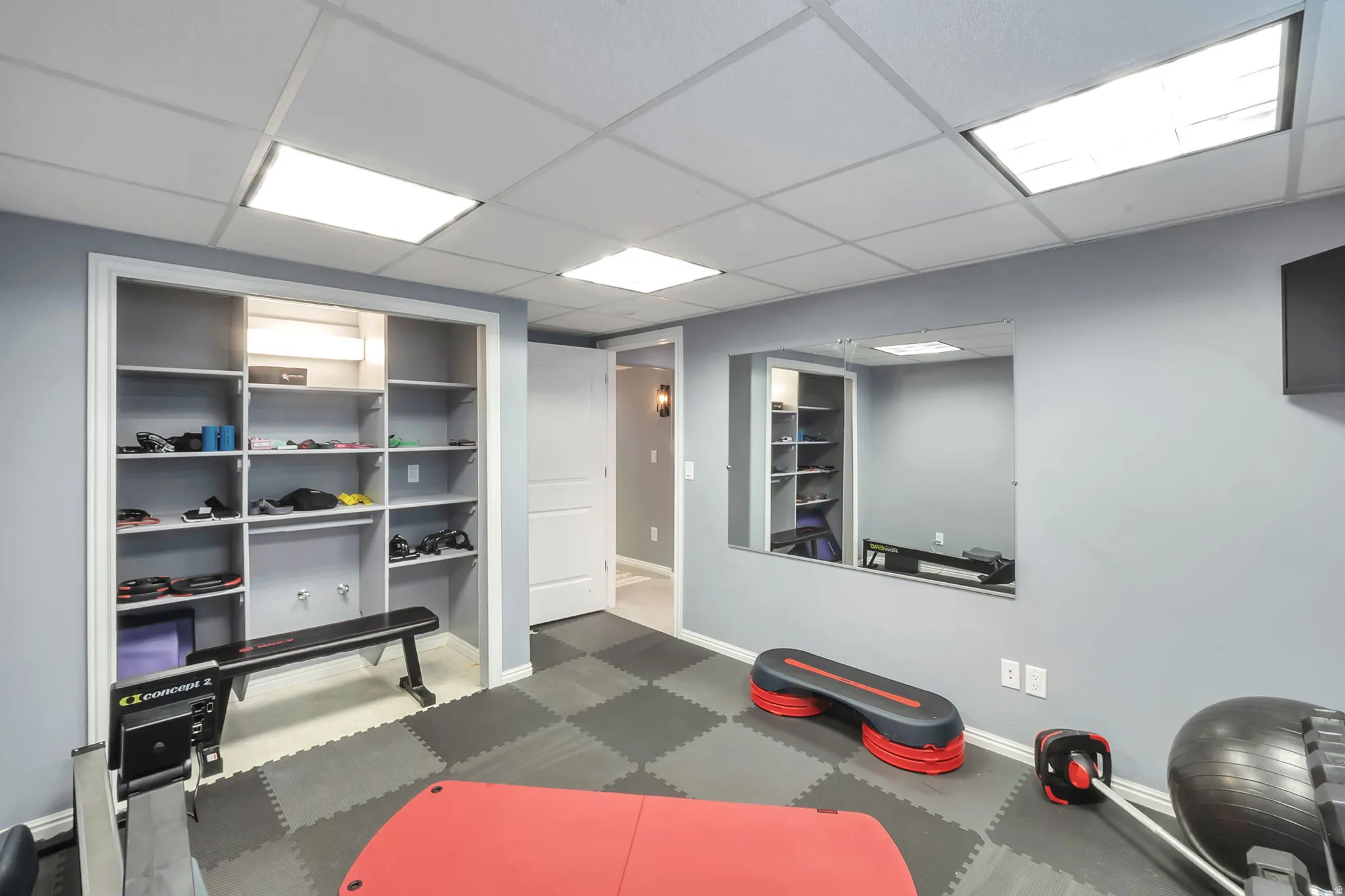 Dedicated activity room featuring a checkerboard-patterned rubber floor, a built-in shelving unit, a large wall-mounted mirror, and recessed ceiling lighting