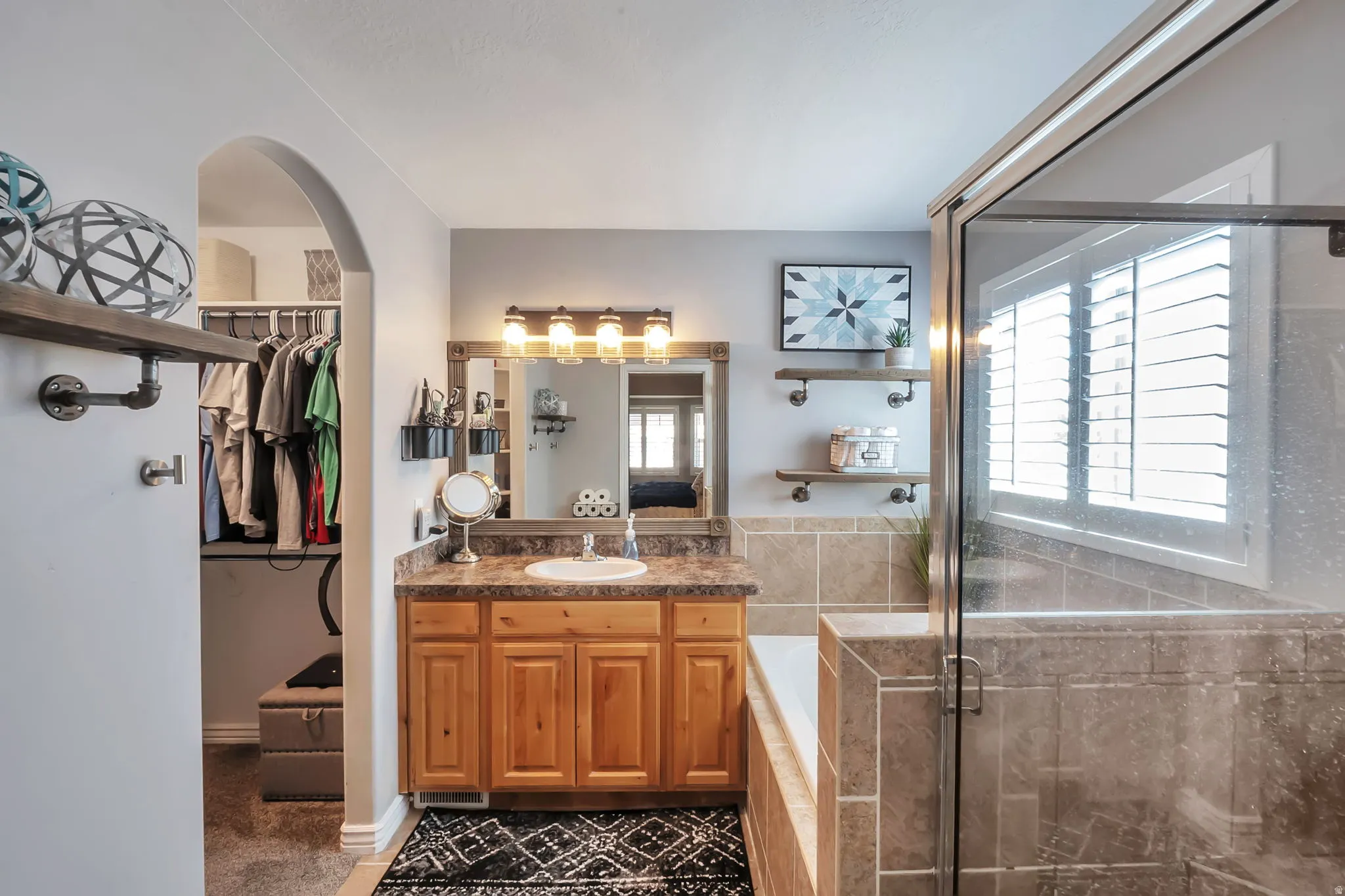Bathroom featuring a wood-finish vanity with a single sink and dark countertop, a glass-enclosed shower, and a built-in tub with tile surround
