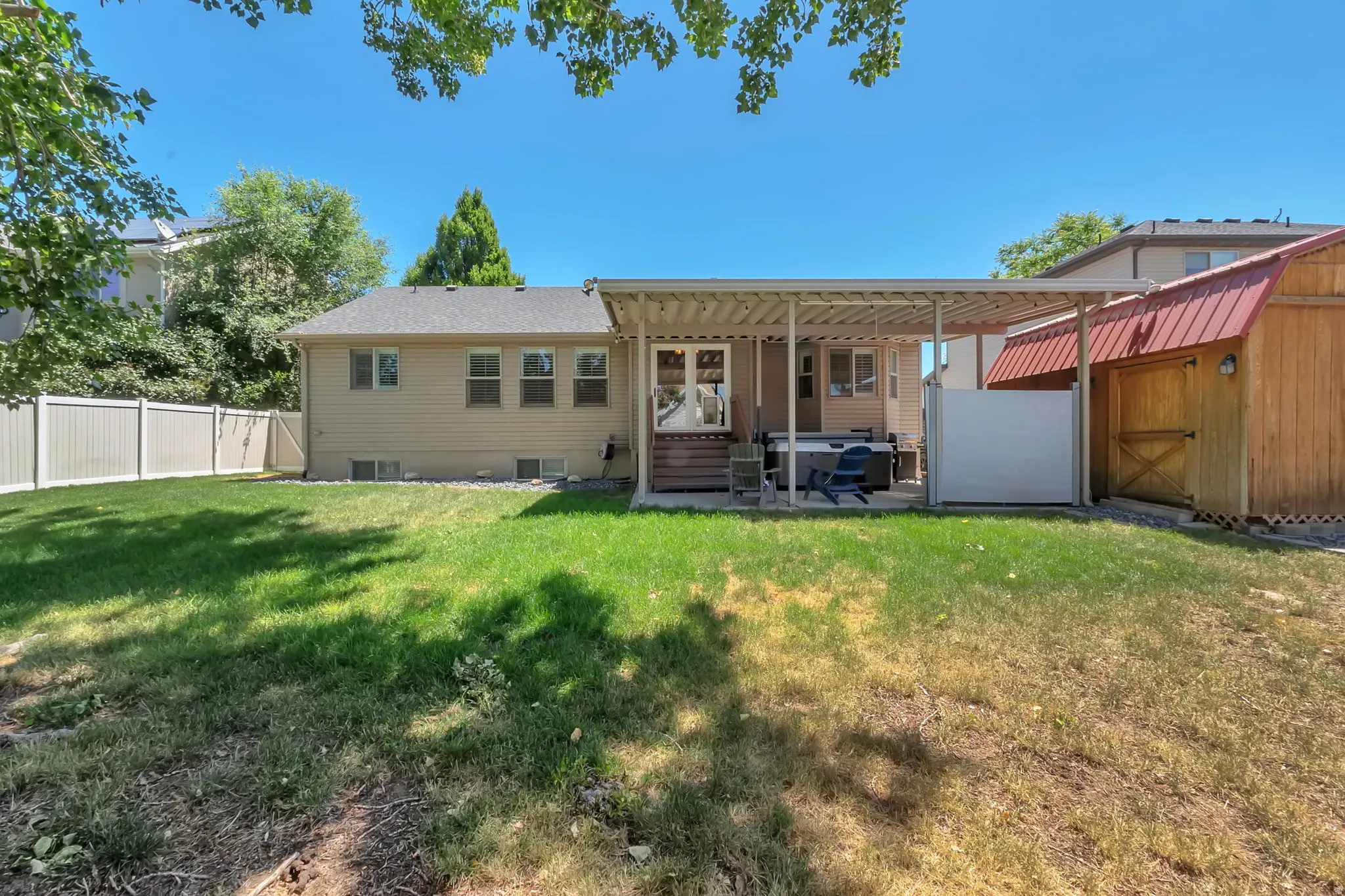 Expansive backyard featuring a covered patio, a detached wooden shed with a red metal roof, and a white privacy fence
