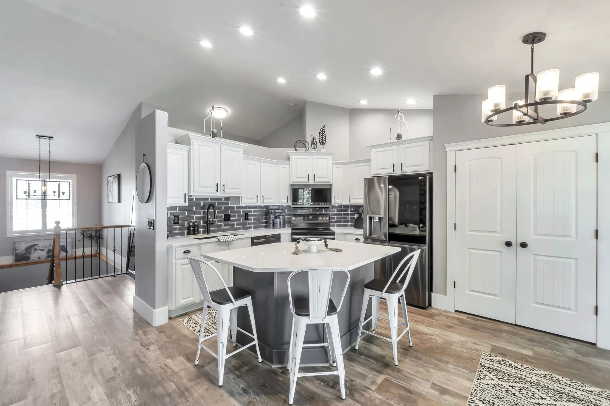 Open-concept kitchen featuring an angular island with a white countertop and seating for four, white cabinetry, a gray subway tile backsplash, stainless steel appliances, and wood-finish flooring