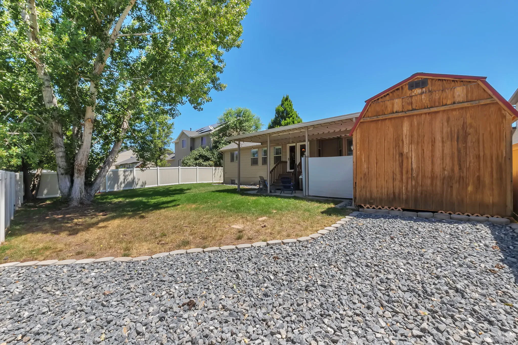 Expansive backyard featuring a gravel area, a wooden storage shed, and a covered patio with an awning