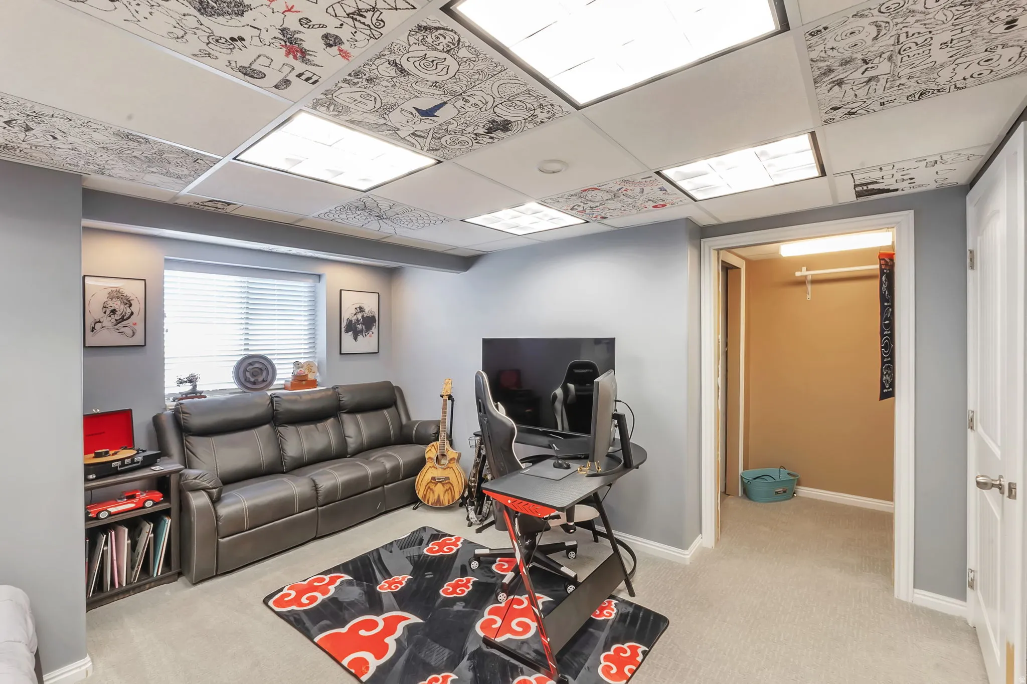 Versatile finished room featuring a drop ceiling with integrated lighting, light gray painted walls, and neutral carpeting