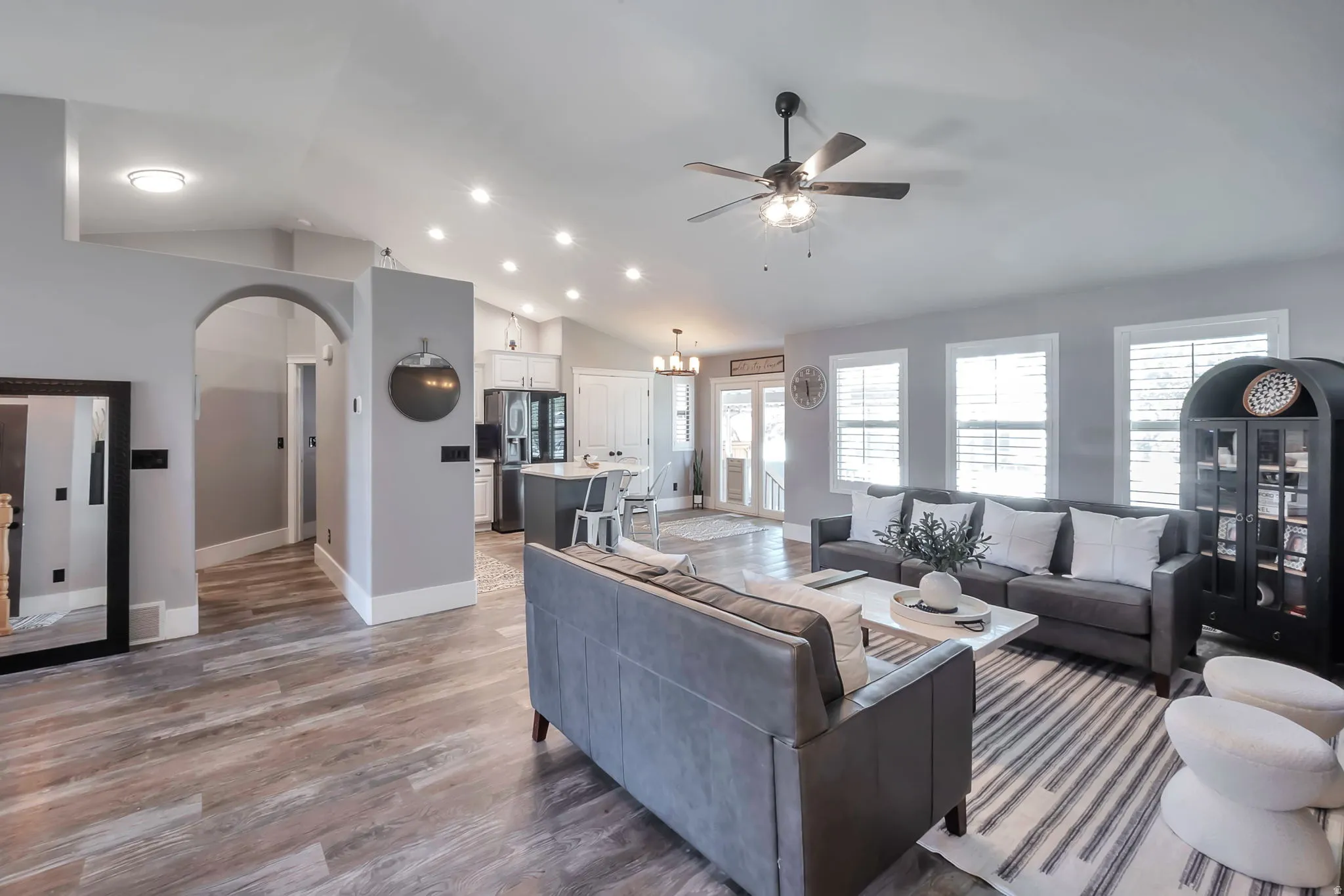 Open-concept living area featuring wood-finish flooring, vaulted ceilings with recessed lighting, and a ceiling fan