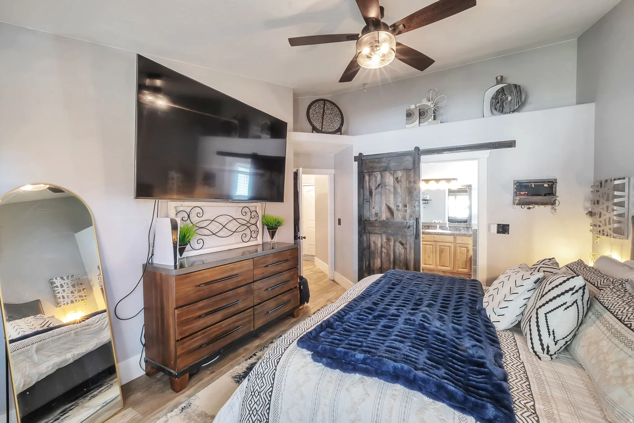Spacious room featuring vaulted ceilings with a wood-finish ceiling fan, wood-finish flooring, and a distressed wood-finish barn door entry to an attached bath
