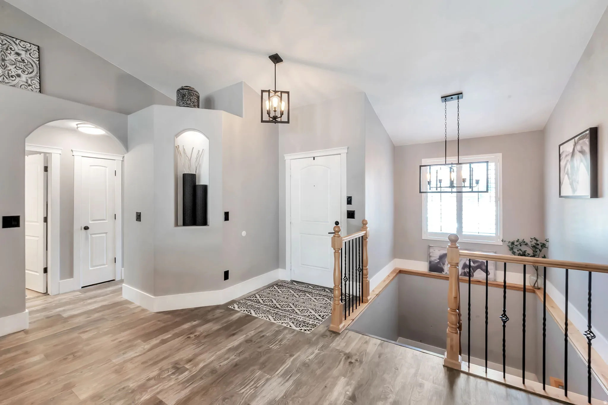 Entryway featuring wood-finish flooring, a contemporary chandelier, a white front door, a built-in display niche, and a staircase with wood handrails and black metal balusters