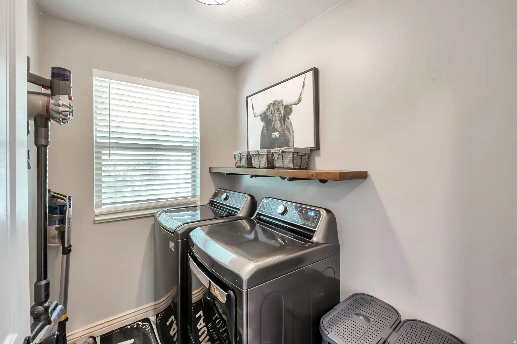Laundry area featuring a window with horizontal blinds, a wood-finish floating shelf, and light-toned wall paint