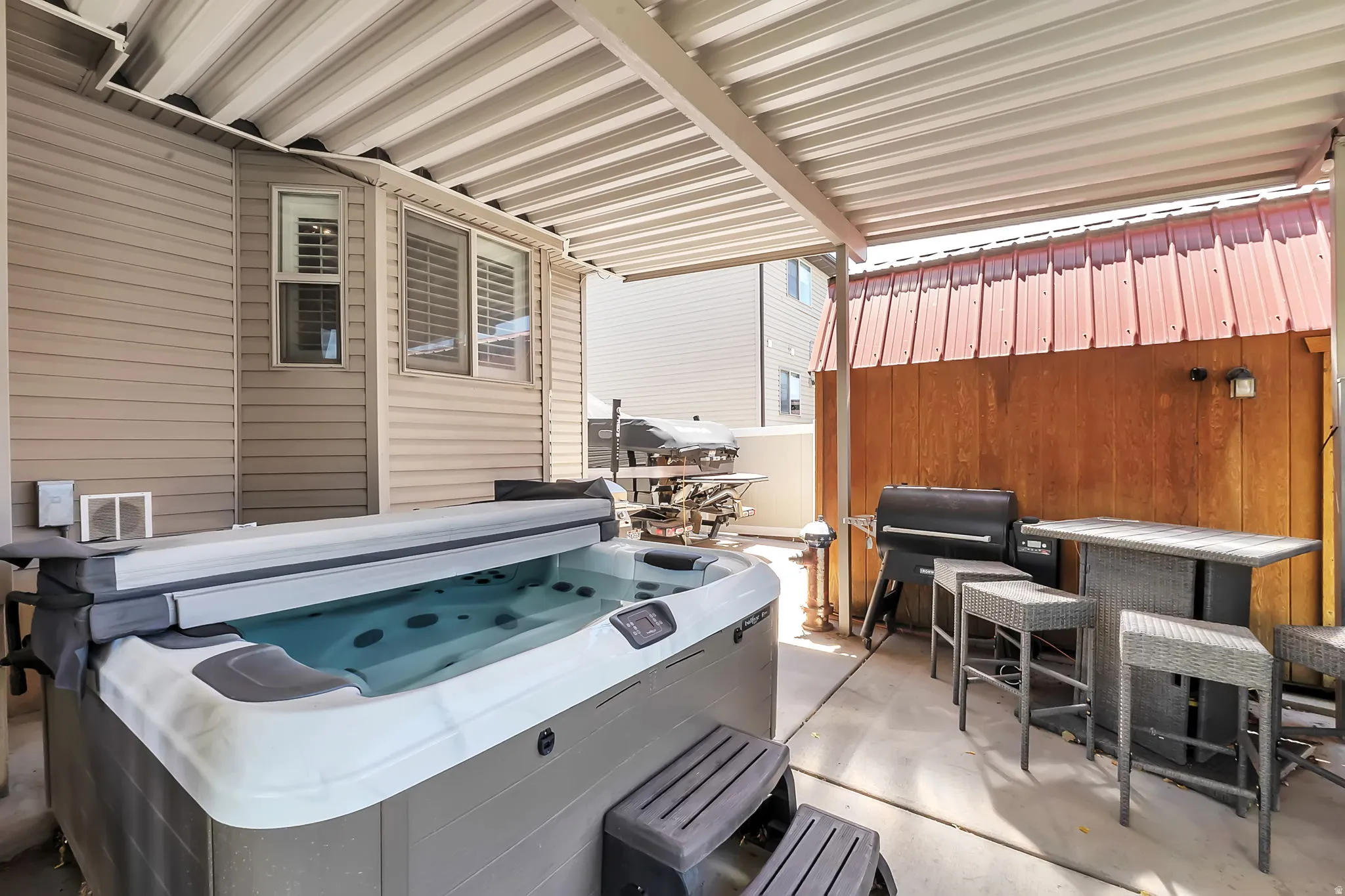 Patio featuring a built-in hot tub, covered outdoor dining area, corrugated metal patio roof, and wood-paneled privacy wall