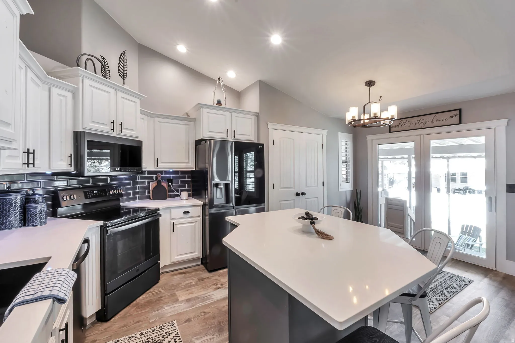 Kitchen featuring an angular island with a white countertop, white cabinetry with dark hardware, a dark subway tile backsplash, stainless steel appliances, and wood-finish flooring
