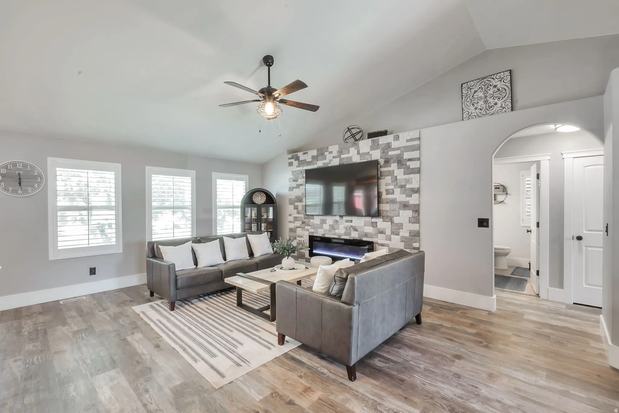 Living room featuring vaulted ceilings, wood-finish flooring, and a ceiling fan