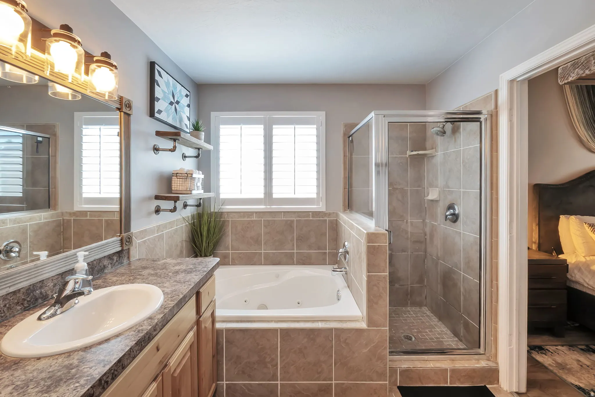 Bathroom featuring a single vanity with an oval sink, a built-in jetted tub, a glass-enclosed shower, tile flooring, and wall-mounted shelving