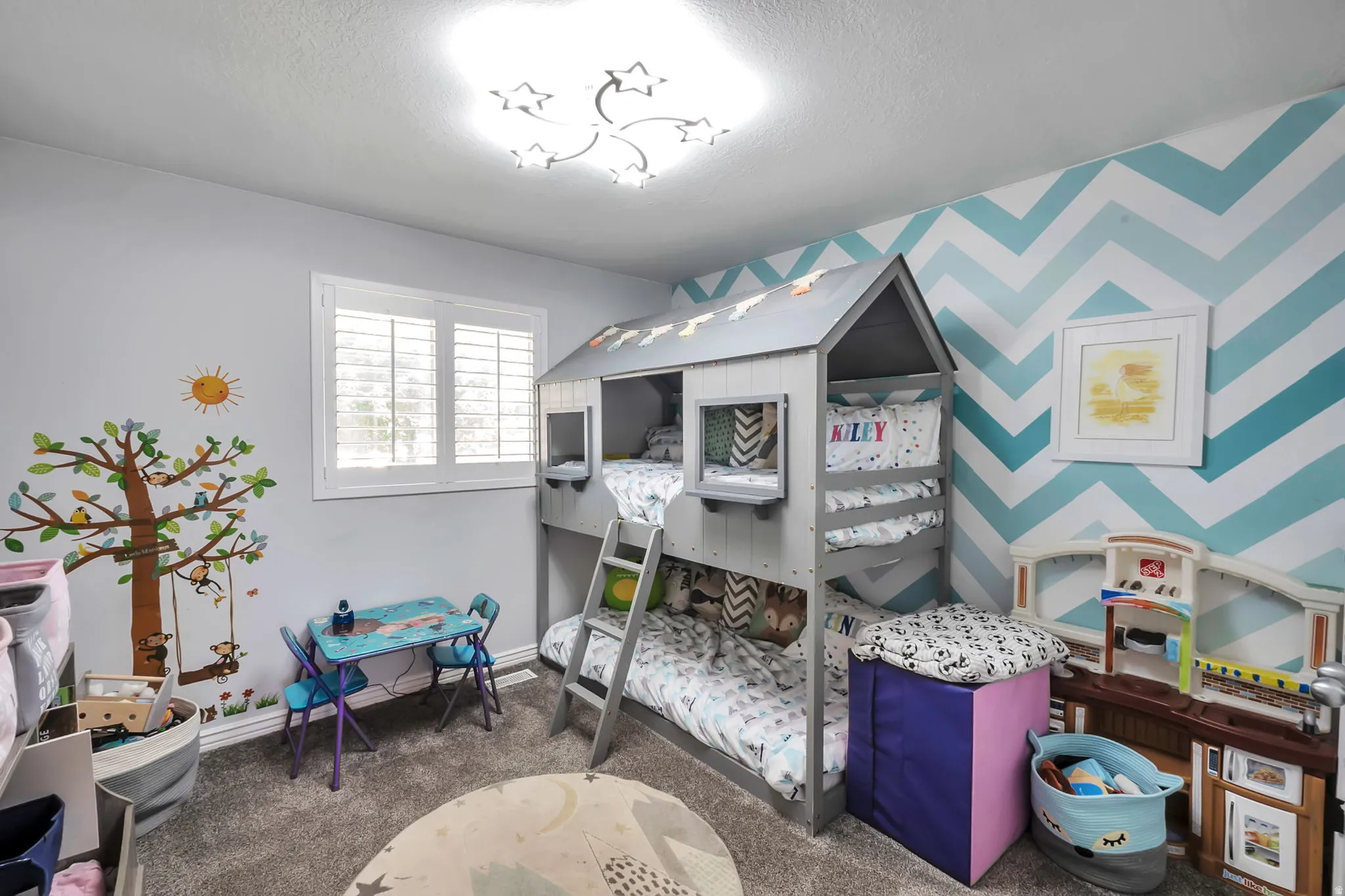 Spacious room featuring a novelty bunk bed, chevron accent wall, plush carpet flooring, a window with plantation shutters, and a star-motif ceiling fixture