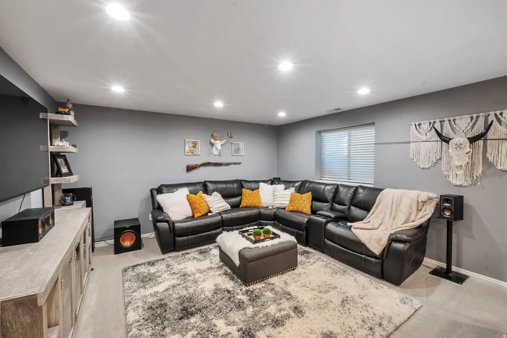 Spacious entertainment room featuring recessed lighting, a large window with horizontal blinds, neutral gray walls, and light-colored carpeting