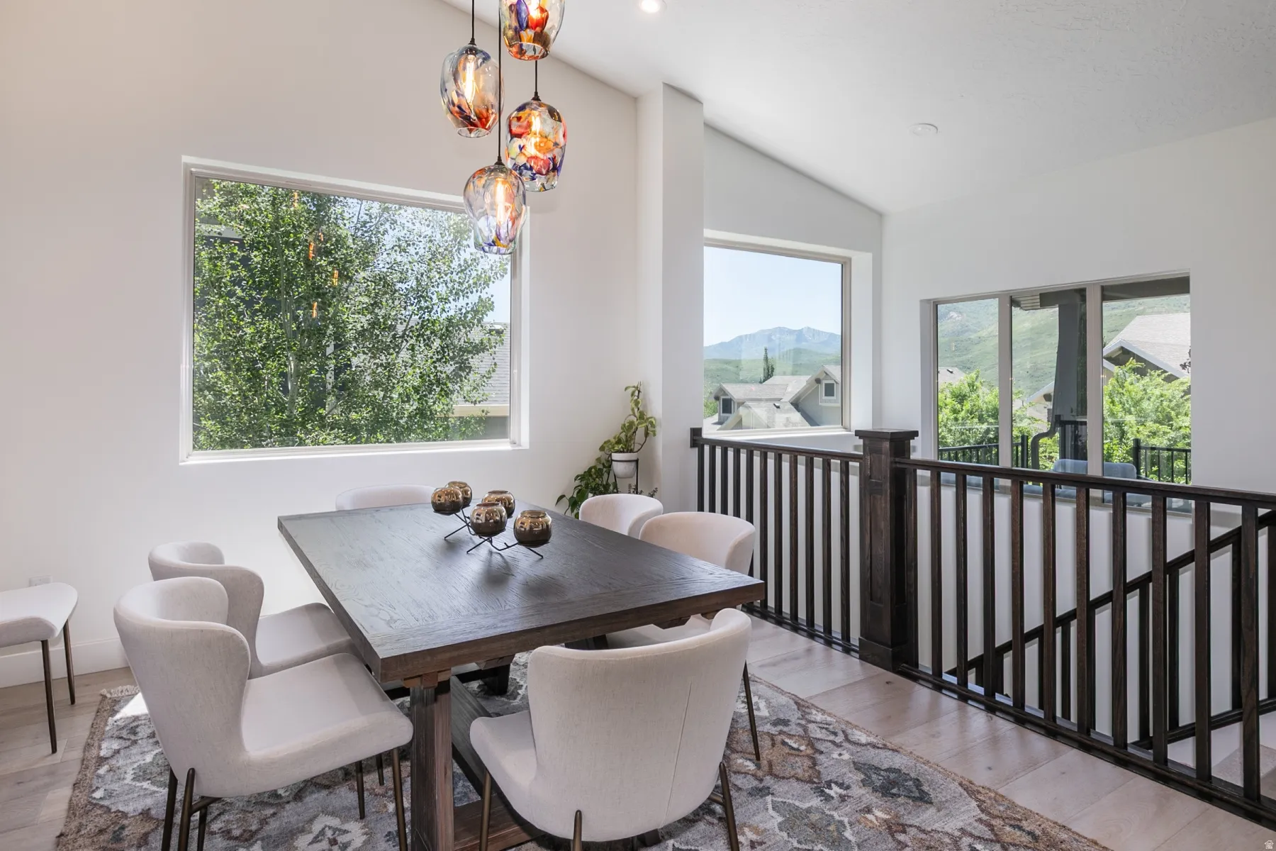 Dining area featuring a modern chandelier with colorful glass pendants, ample natural light from multiple windows, and light wood-finish flooring