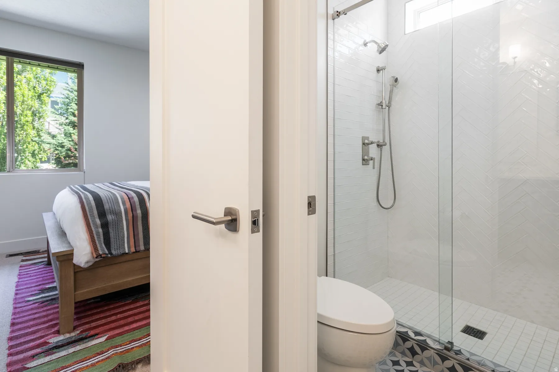 Modern bathroom featuring a glass-enclosed shower with white herringbone tile and a rain shower head