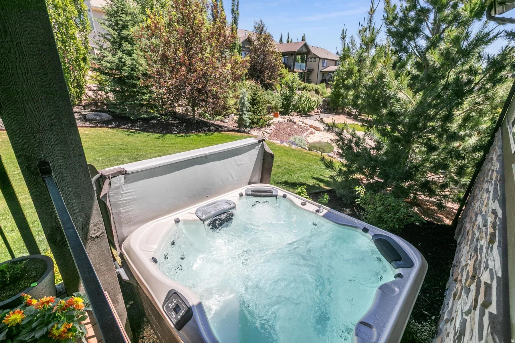 Outdoor spa with integrated jets, surrounded by mature trees, a manicured lawn, and natural stone landscaping