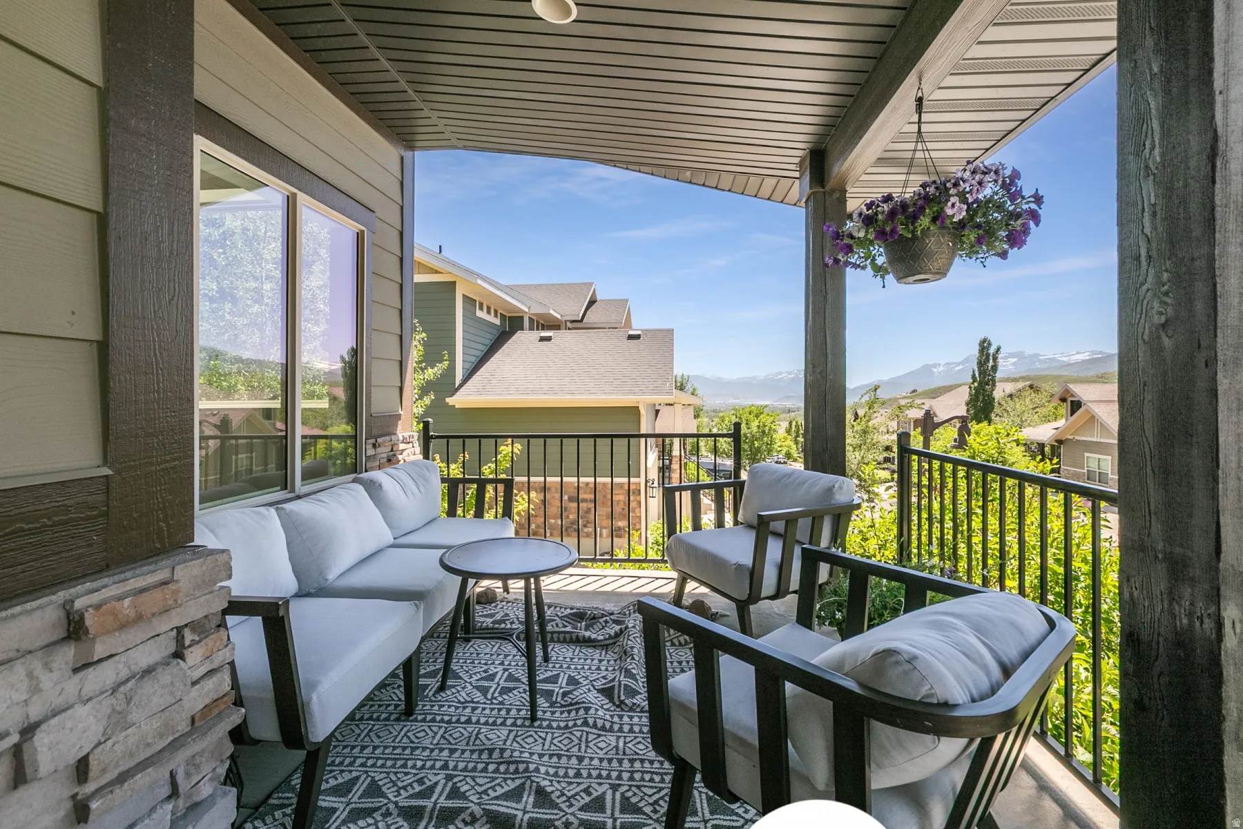 Covered outdoor patio featuring a stone veneer accent column, horizontal siding, and a black metal railing