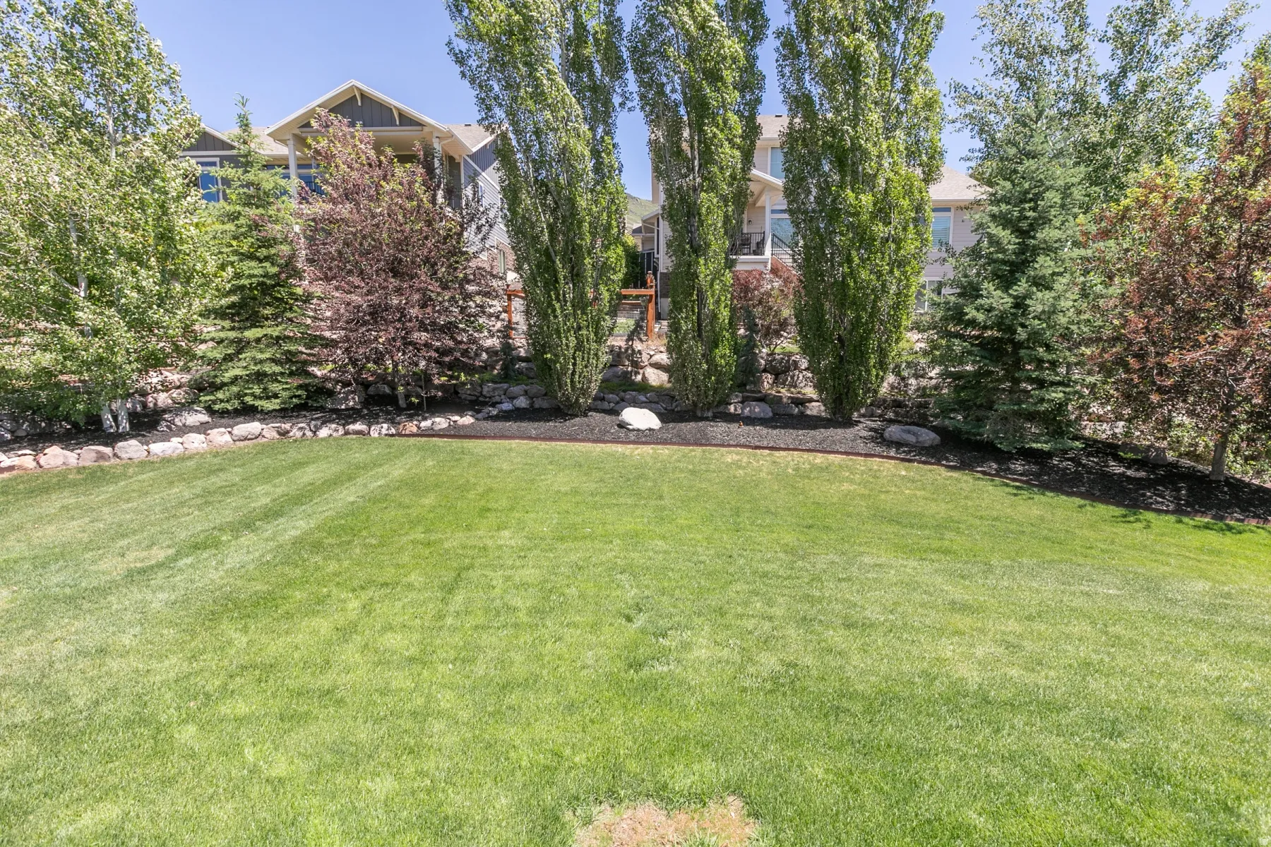 Expansive lawn area with a defined perimeter, mature trees, and natural stone retaining walls
