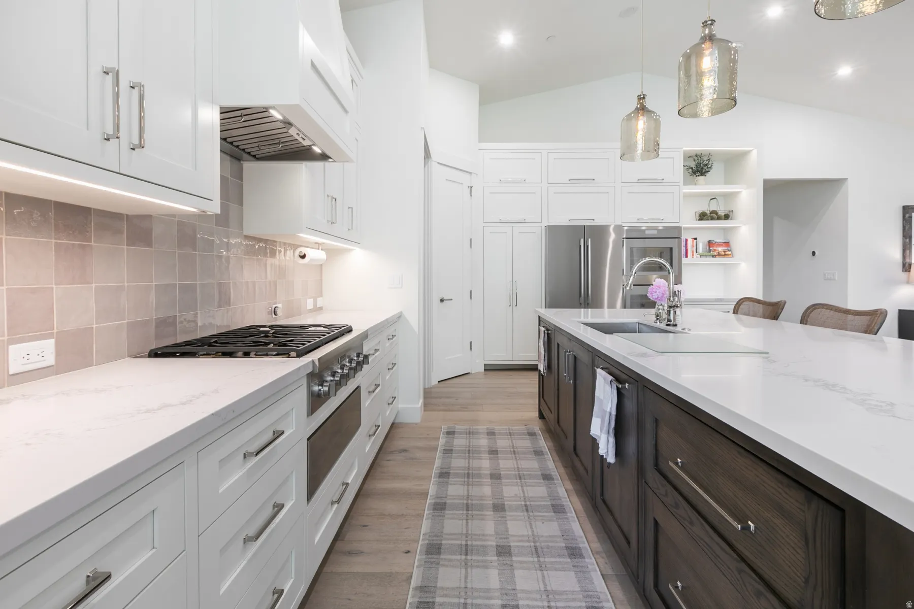 Gourmet kitchen featuring a large central island with integrated sink, stainless steel appliances, extensive white cabinetry, quartz countertops, and wood-finish flooring