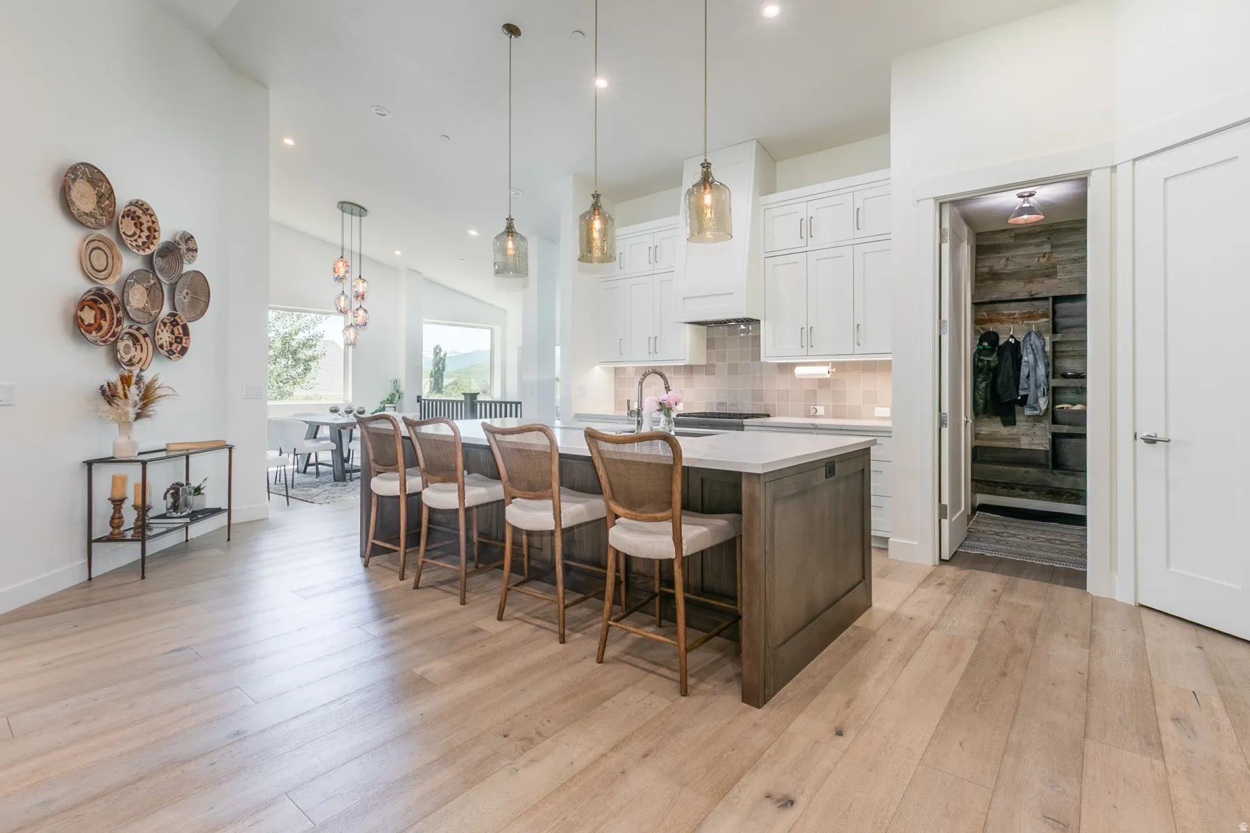 Bright kitchen featuring a substantial island with seating, pendant lighting, white cabinetry, and wood-finish flooring