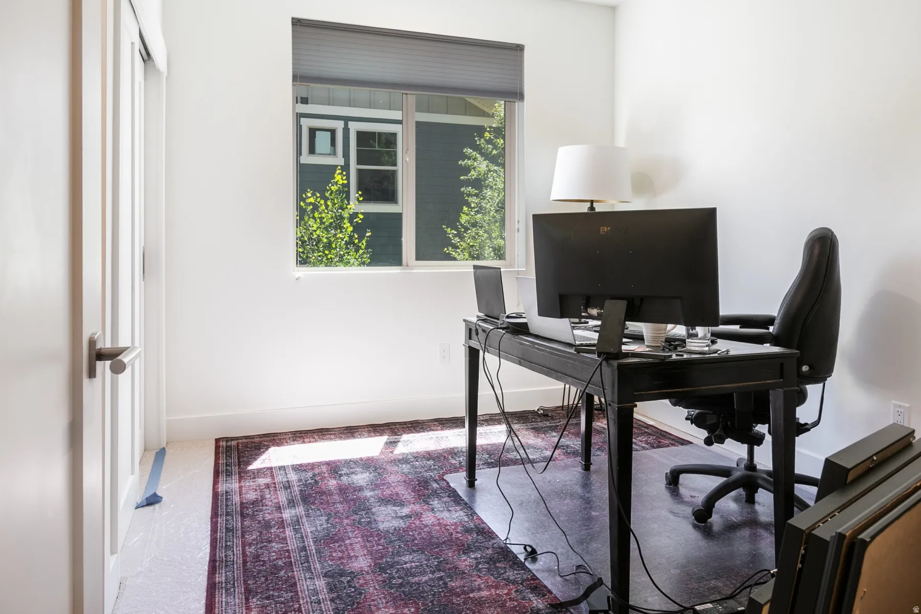 Bright room featuring a window with a roller shade, light-colored walls, and a white door with a brushed nickel handle