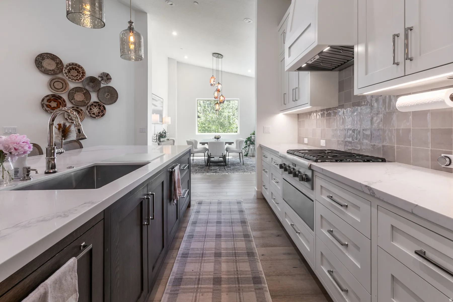 Gourmet kitchen featuring a large island with an undermount sink, gas range with a professional-grade hood, white shaker cabinetry, and wood-finish flooring