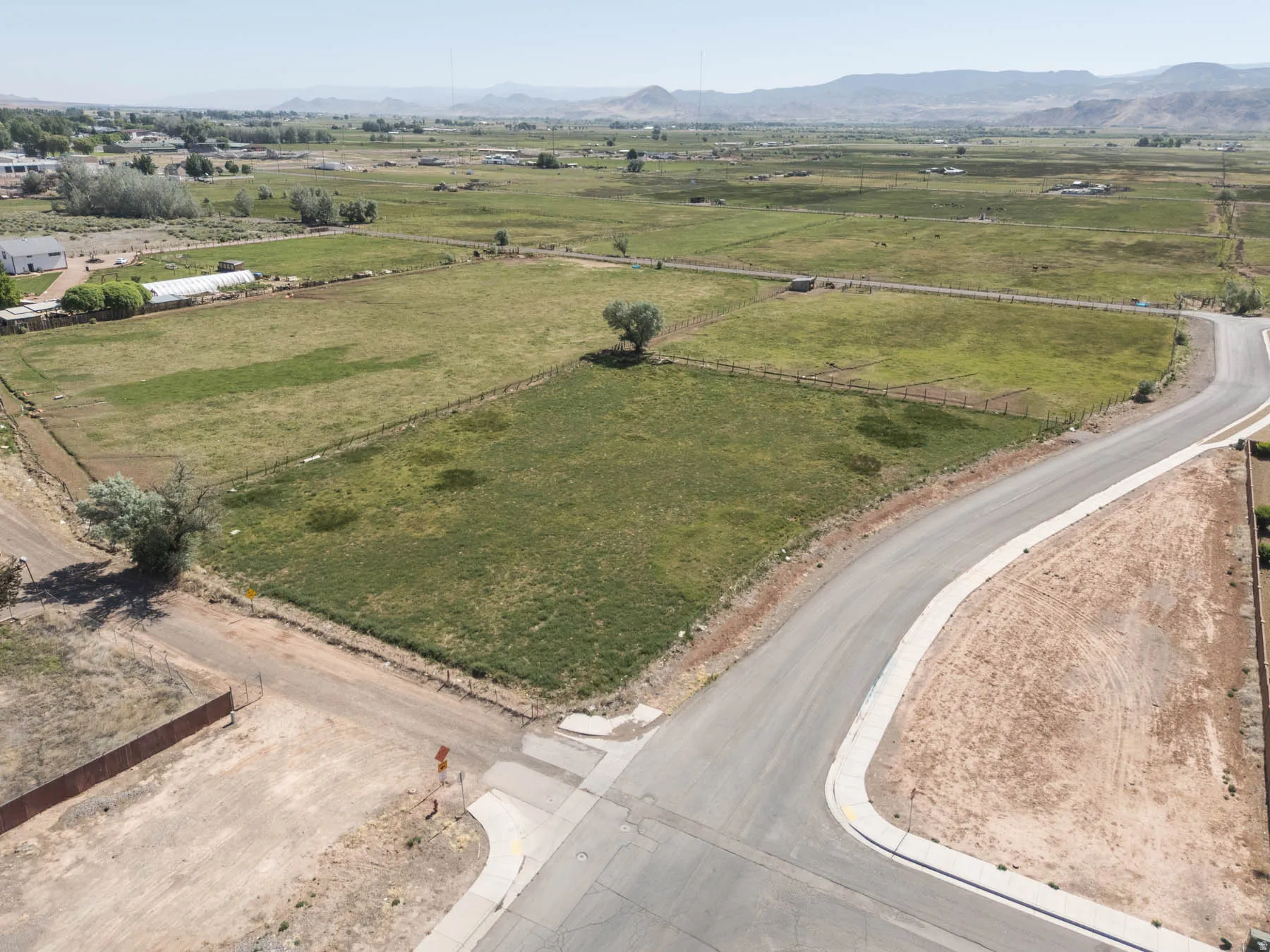 Expansive rural landscape featuring a paved street, established fencing, and distant mountains
