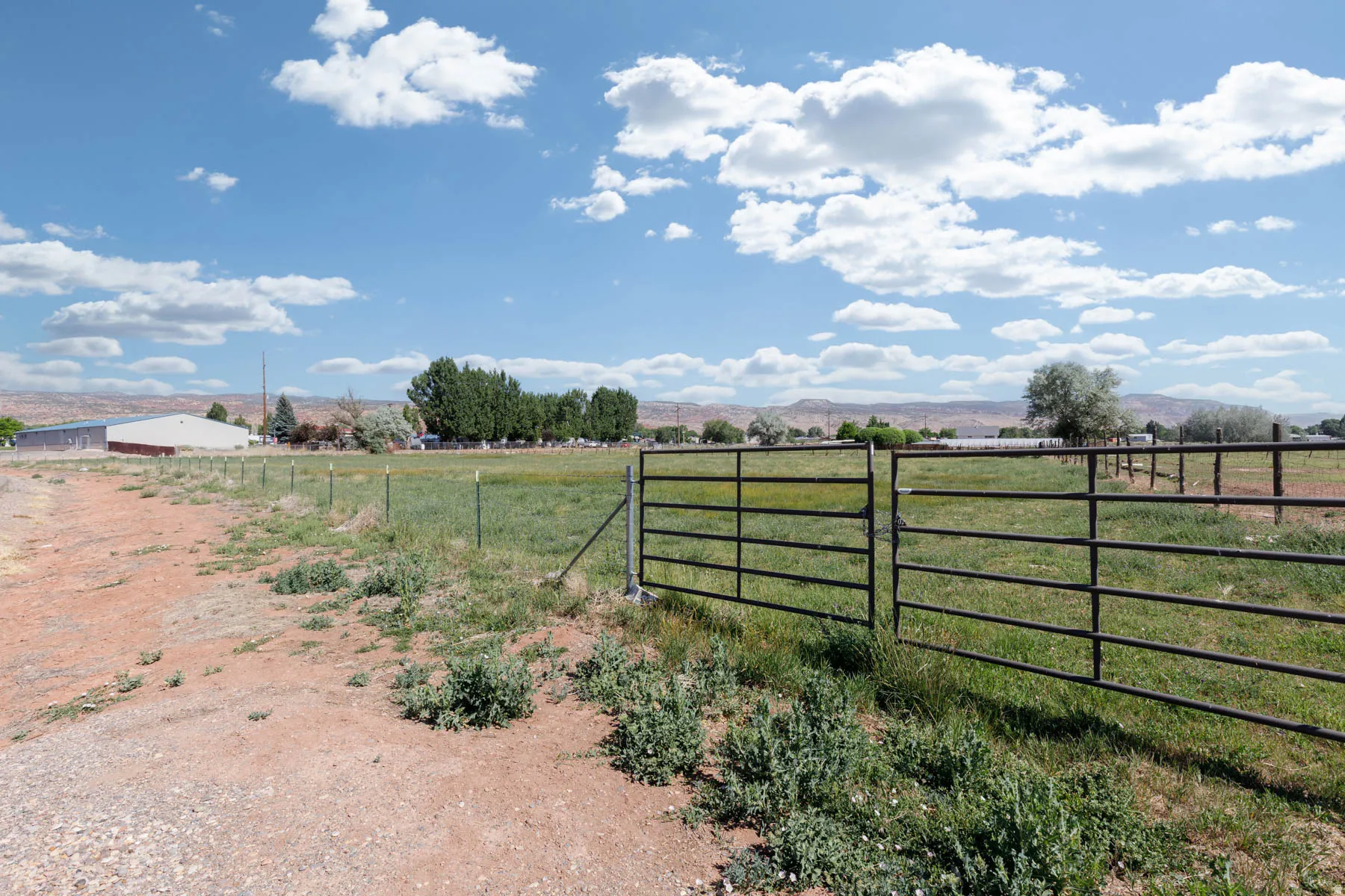 Expansive open field featuring a black metal gate and perimeter fencing