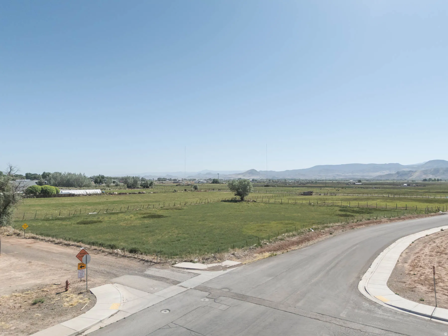 Expansive rural landscape featuring green fields, distant mountains, and a clear sky