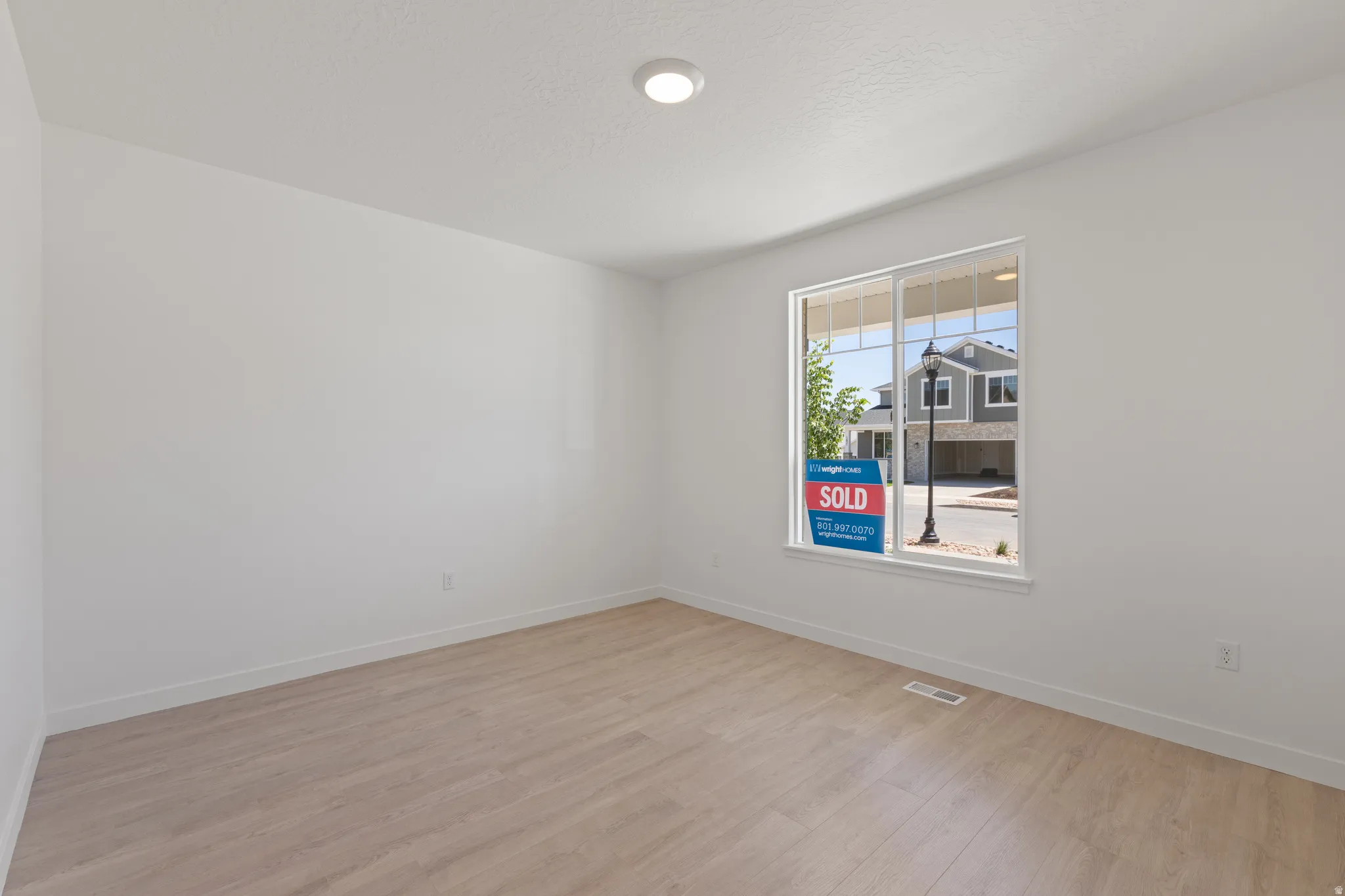 Spacious room featuring light wood-finish flooring, white walls, and a large window