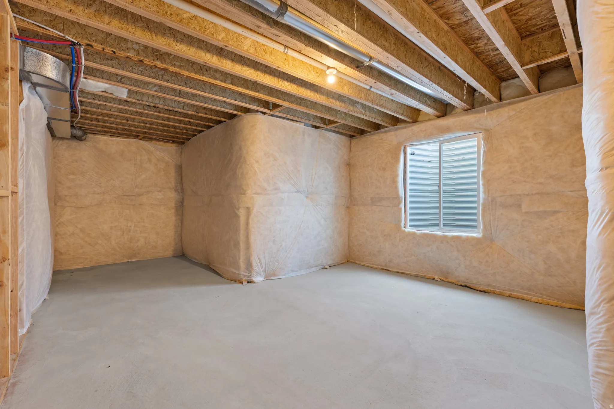 Unfinished basement featuring exposed wood joists, concrete flooring, insulated walls, and a single window