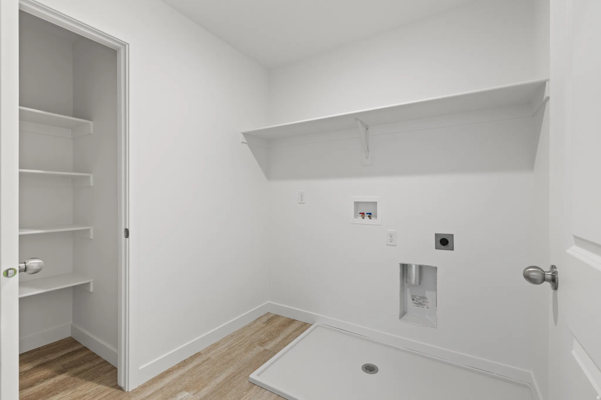 Dedicated laundry room featuring wood-finish flooring, a built-in utility sink base, and overhead shelving