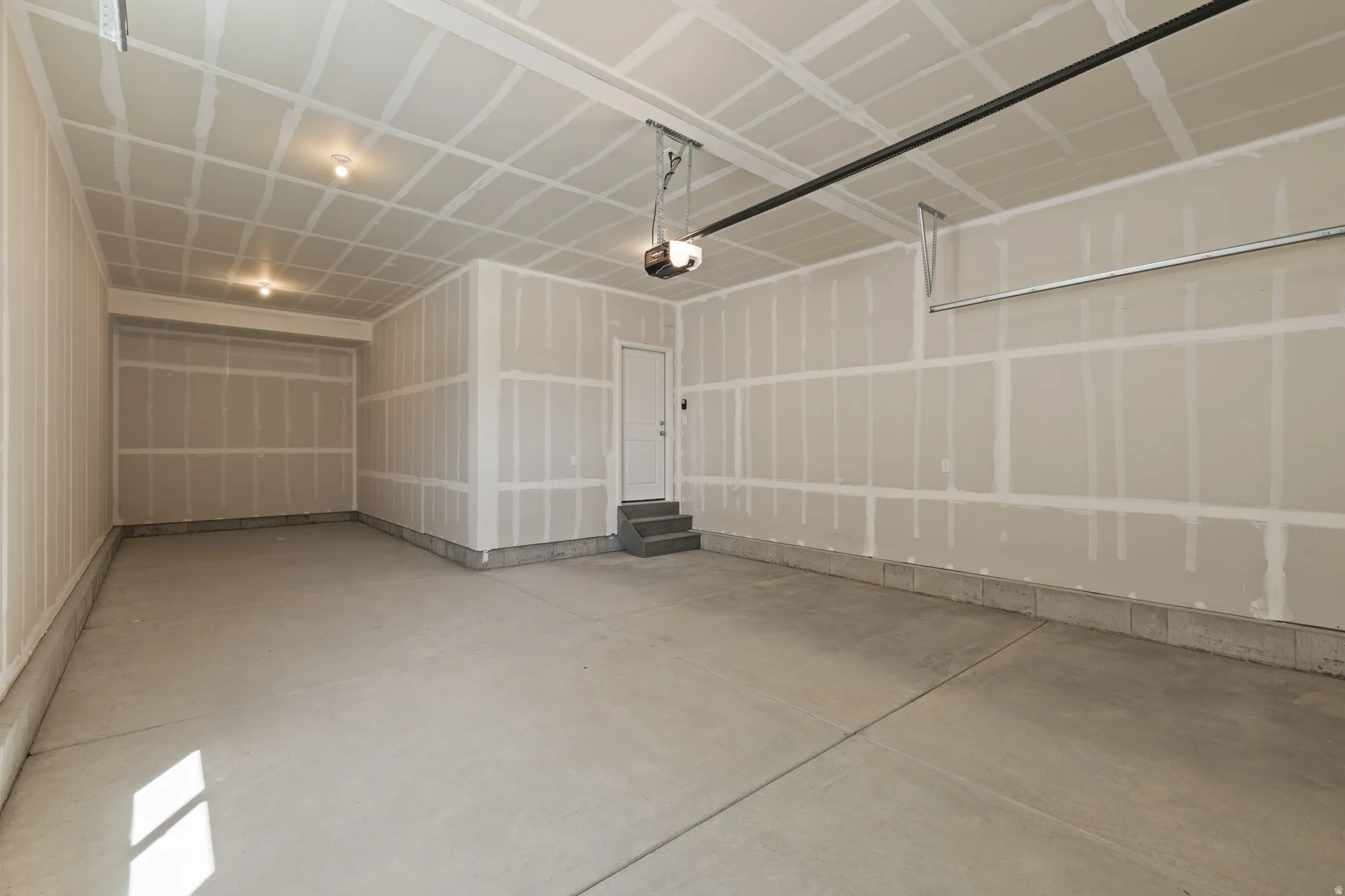 Spacious garage featuring a concrete floor, exposed drywall walls, and a ceiling with two recessed light fixtures