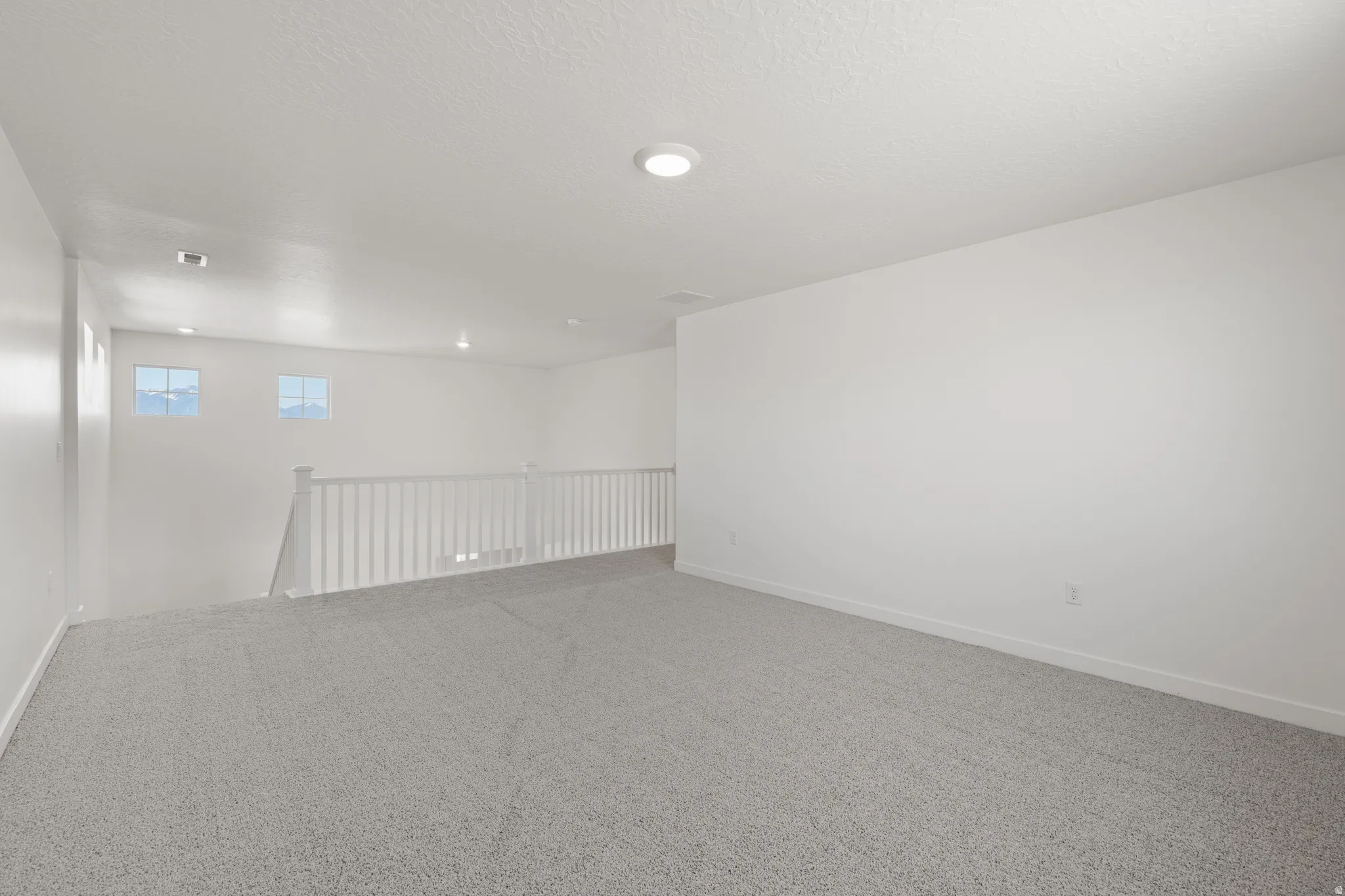 Spacious loft area featuring light gray carpet flooring and white painted walls
