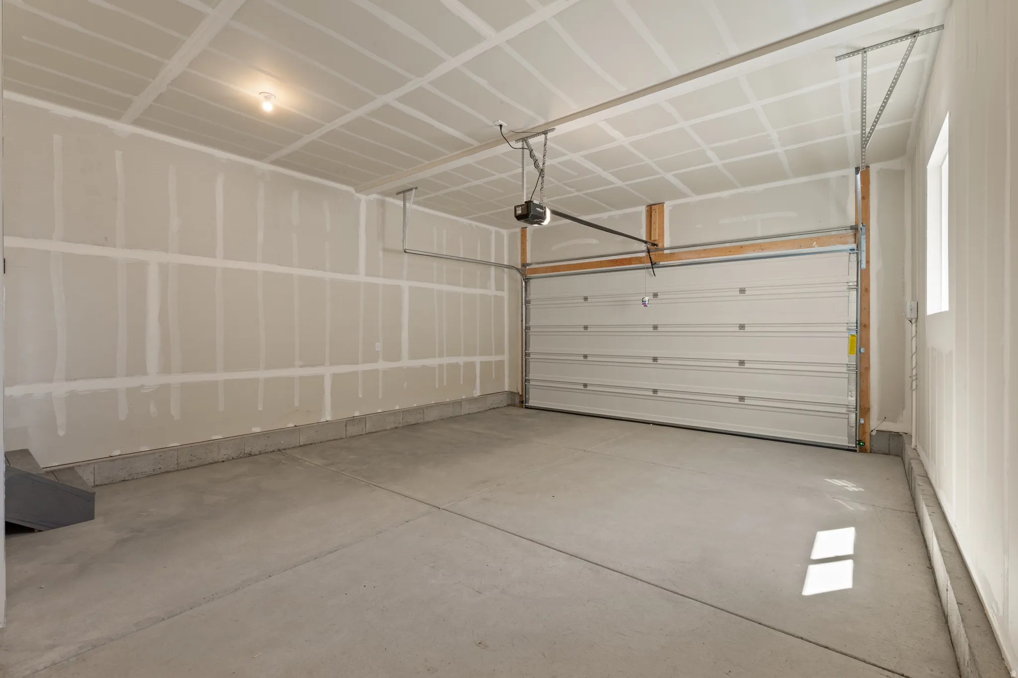 Spacious two-car garage featuring a concrete floor, an overhead garage door, built-in garage door opener, and a single window for natural light
