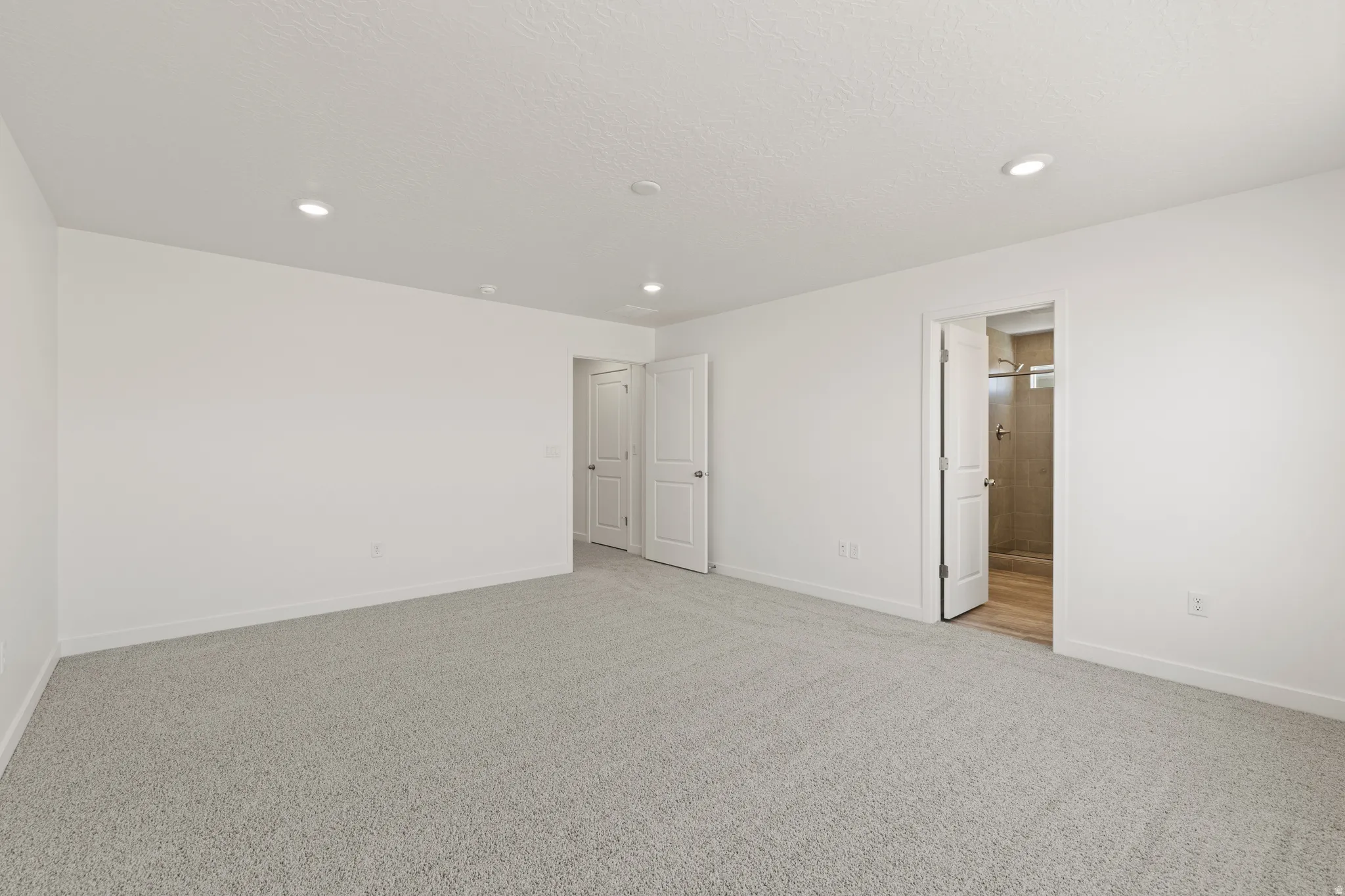 Spacious room featuring light gray carpeting, crisp white walls, and recessed lighting