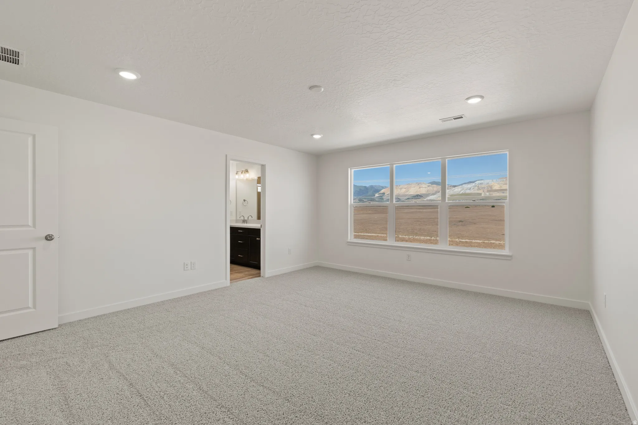 Expansive room featuring multiple windows framing a mountain backdrop, neutral carpeting, recessed lighting, and a white interior door