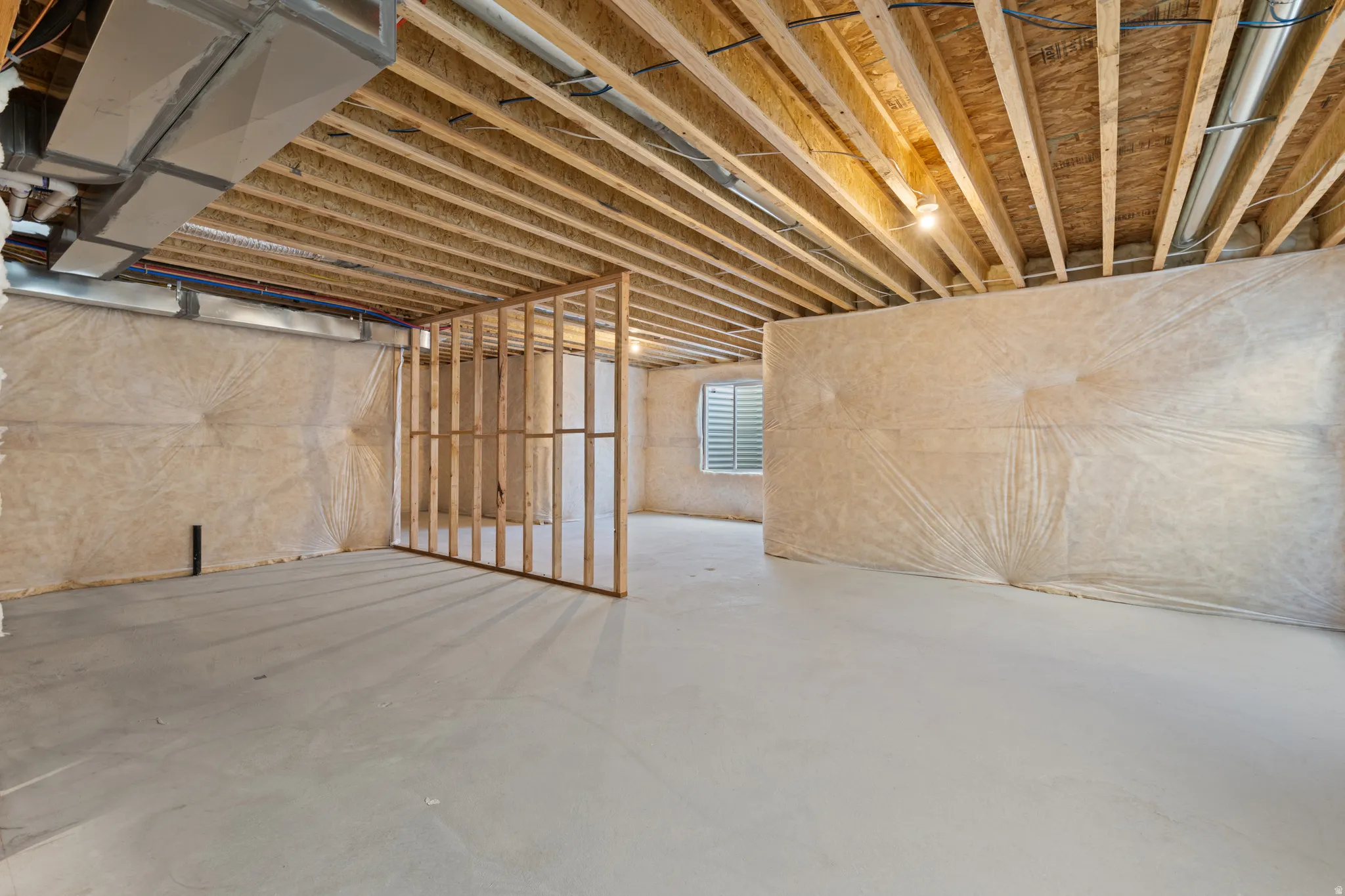 Unfinished basement featuring exposed wood joists, concrete flooring, insulated walls, and a framed partition